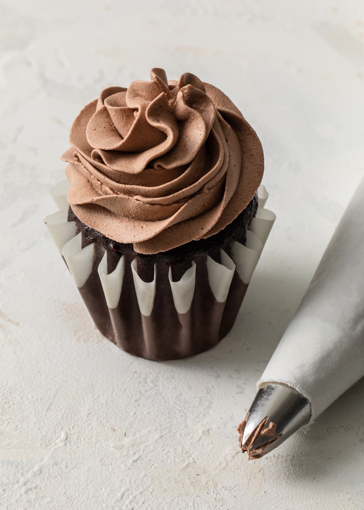 A single chocolate cupcakes with chocolate whipped cream swirled on top with a piping bag