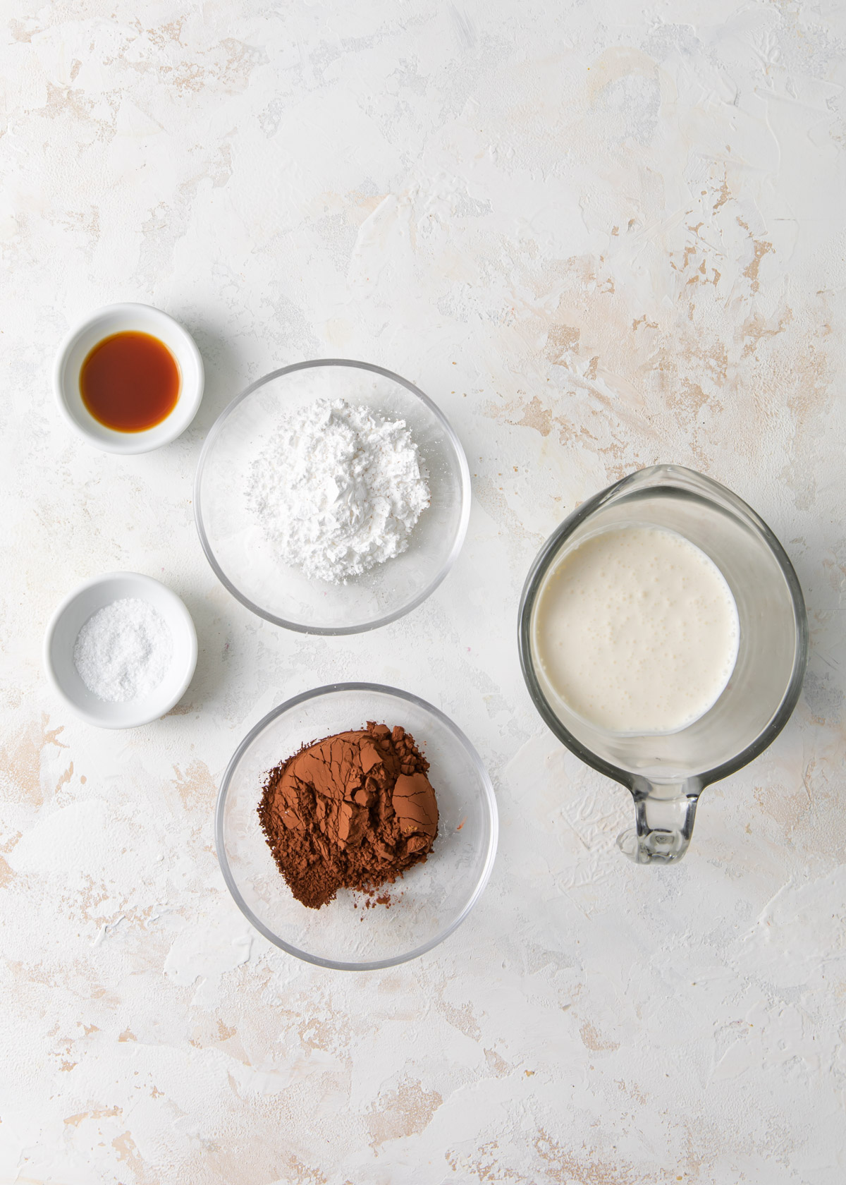 5 ingredients for making chocolate whipped cream on a white table