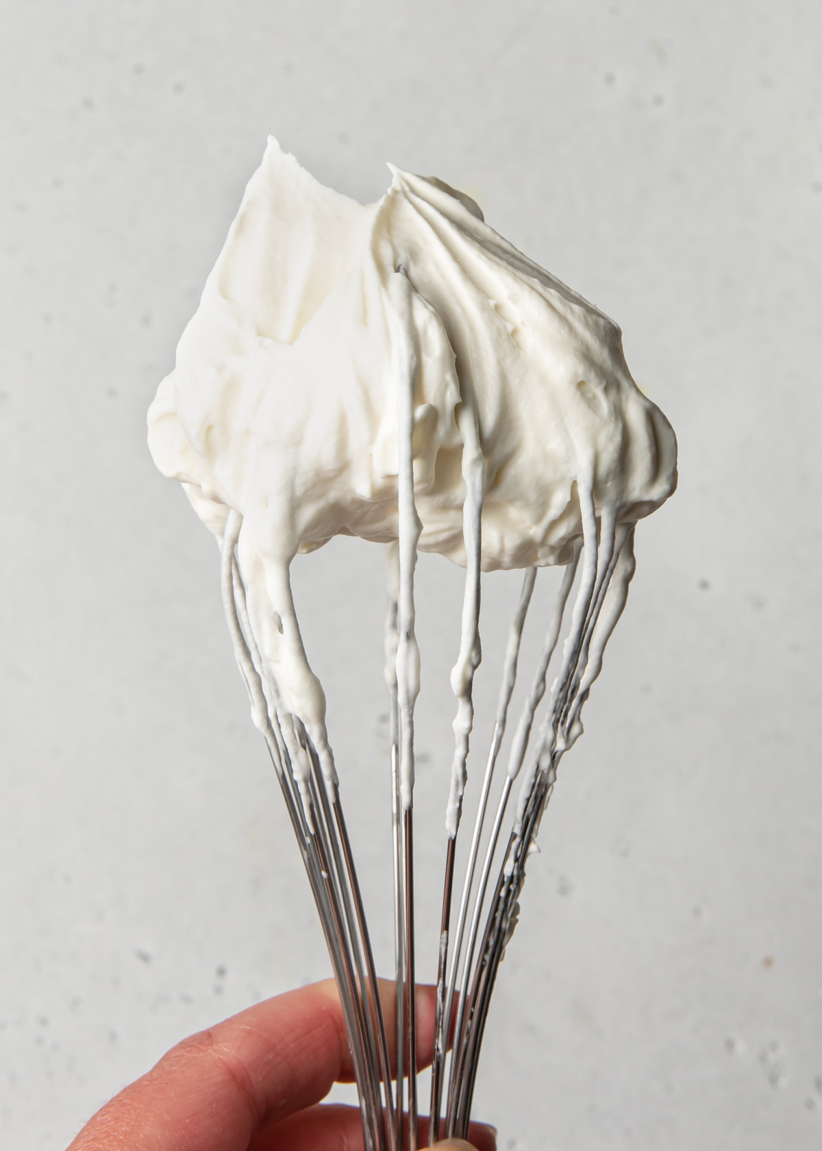 A whisk showing whipped cream stiff peaks