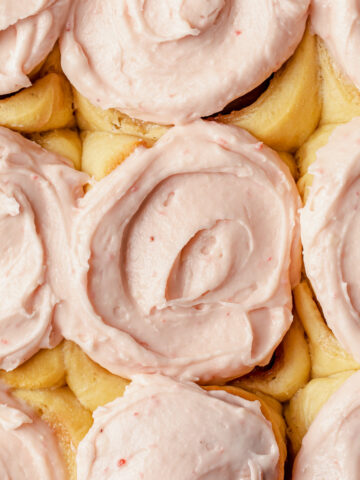 A close-up of strawberry cream cheese frosting spread on top of cinnamon rolls