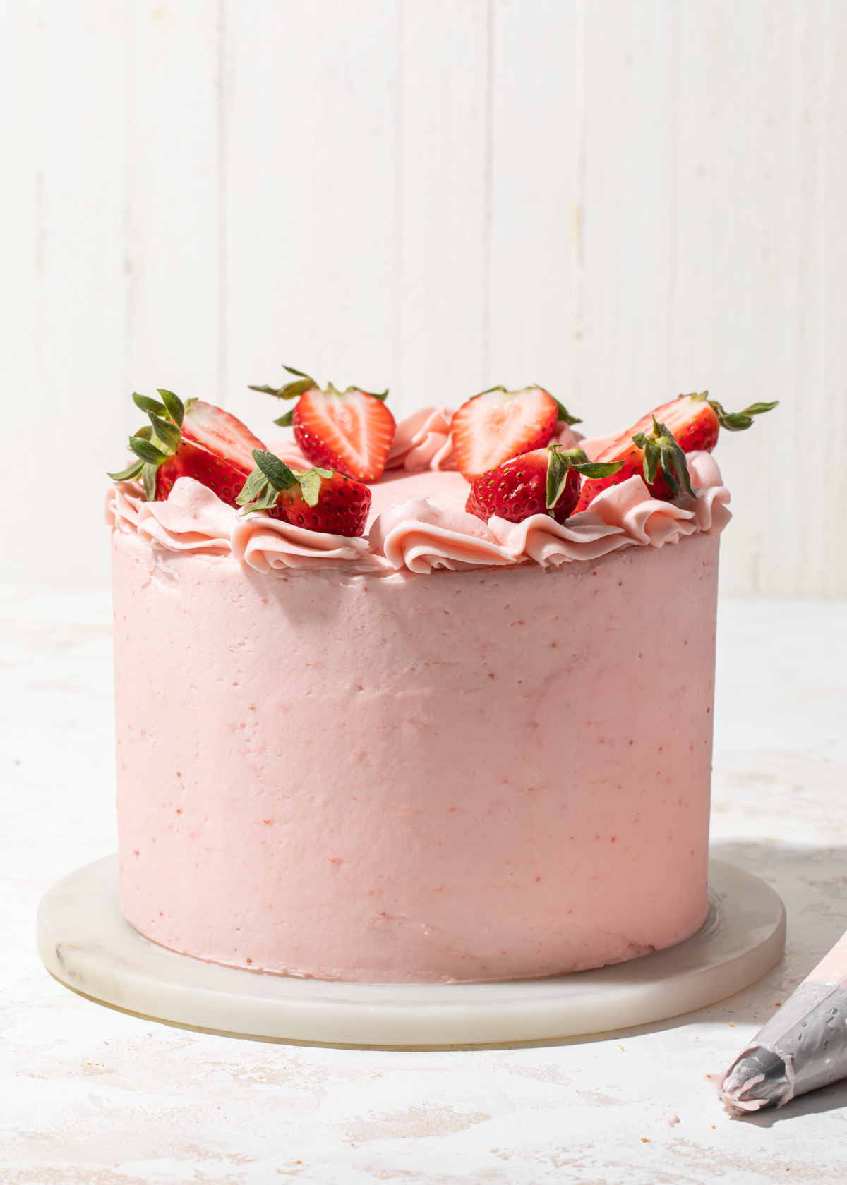 A pink strawberry butter cream cake with fresh strawberries on top