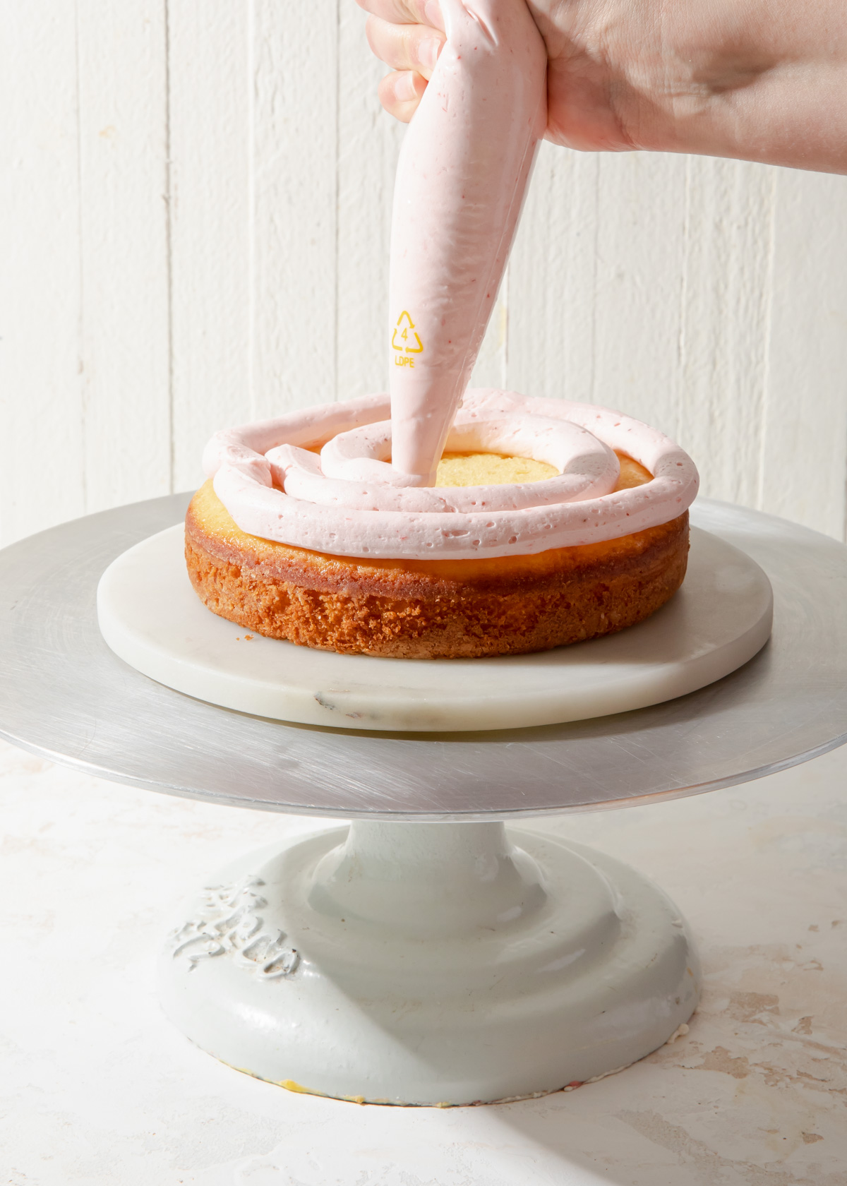 Piping strawberry buttercream onto a vanilla cake