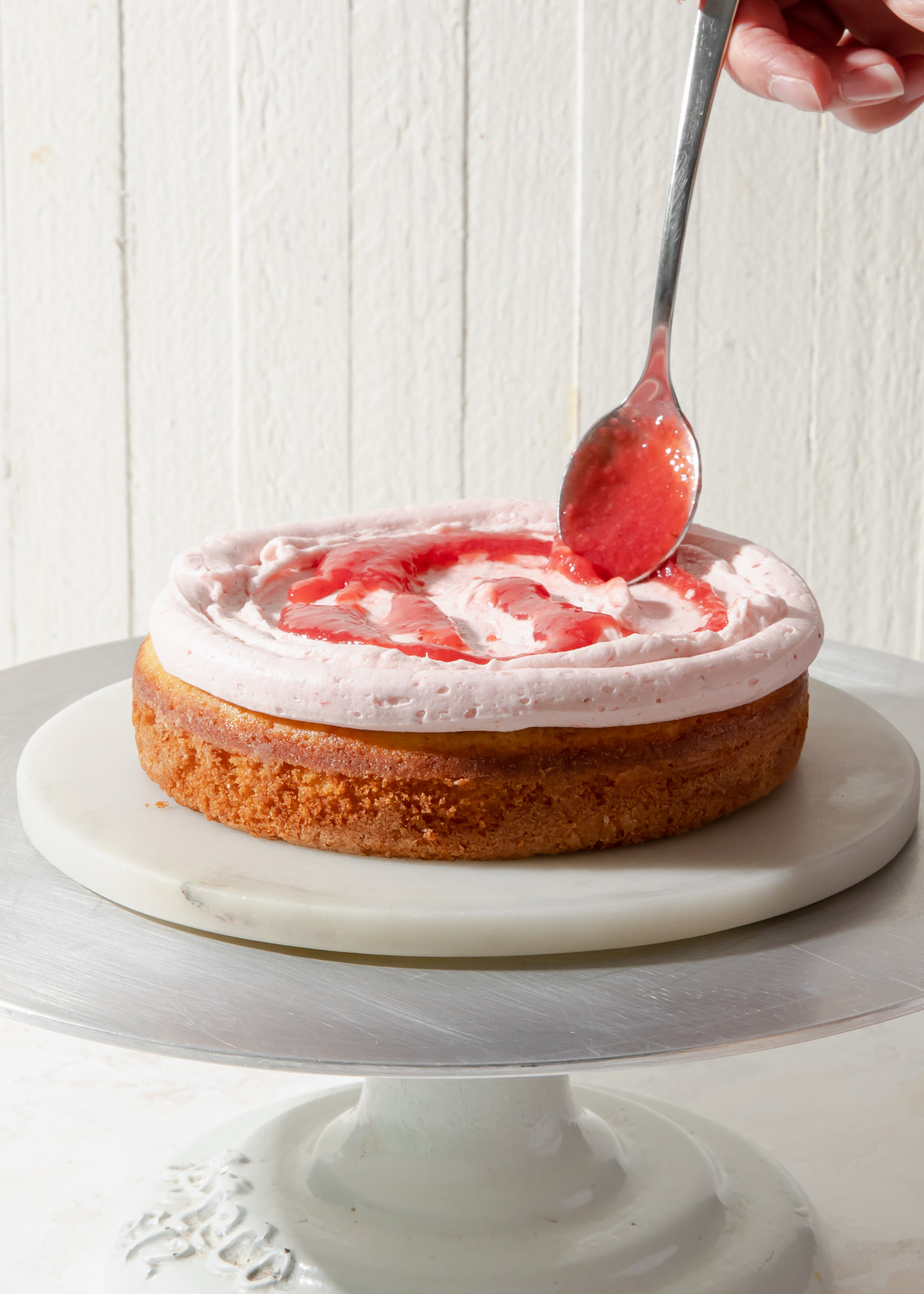 Spooning strawberry filling onto a vanilla cake