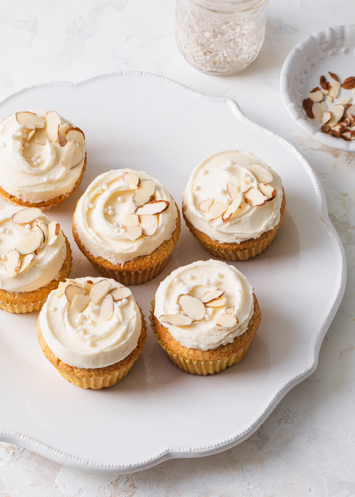 A white platter of cupcakes with almond buttercream and sliced almonds on top