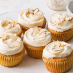 A white platter of cupcakes with almond buttercream and sliced almonds on top