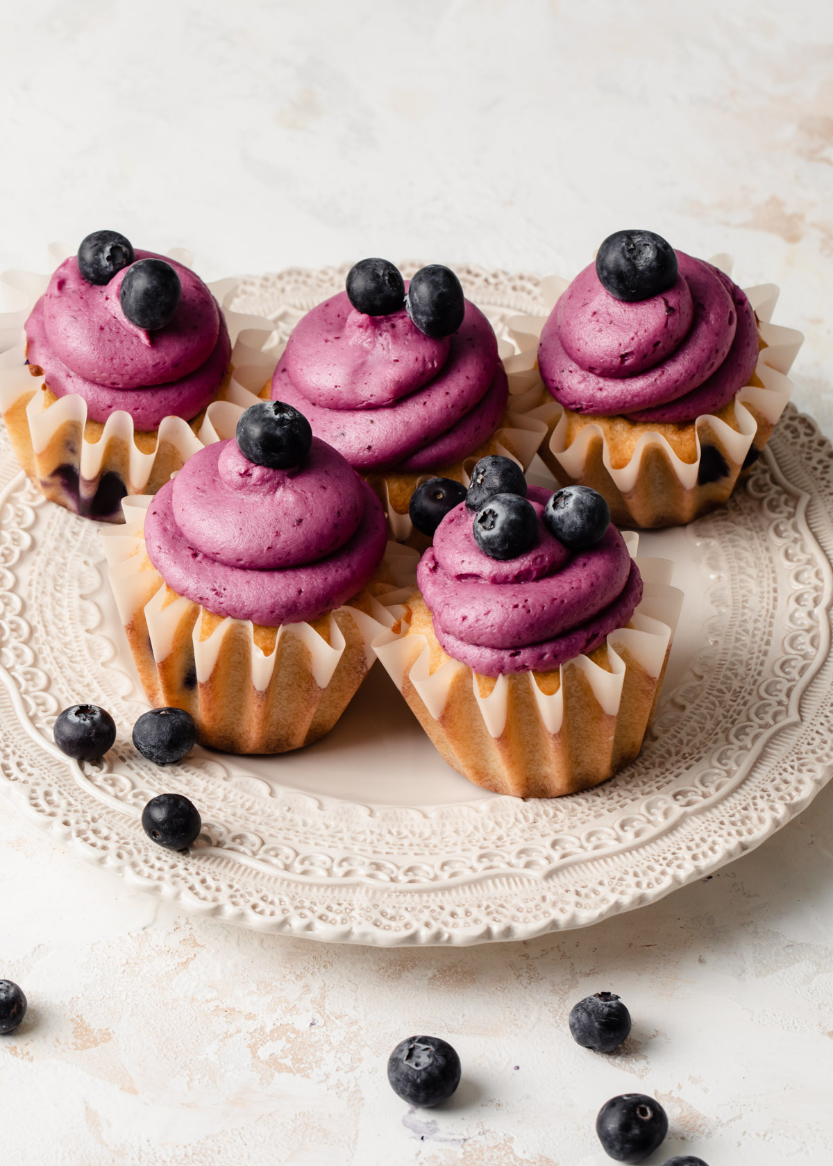 A plater of cupcakes with purple blueberry buttercream swirled on top and fresh blueberries