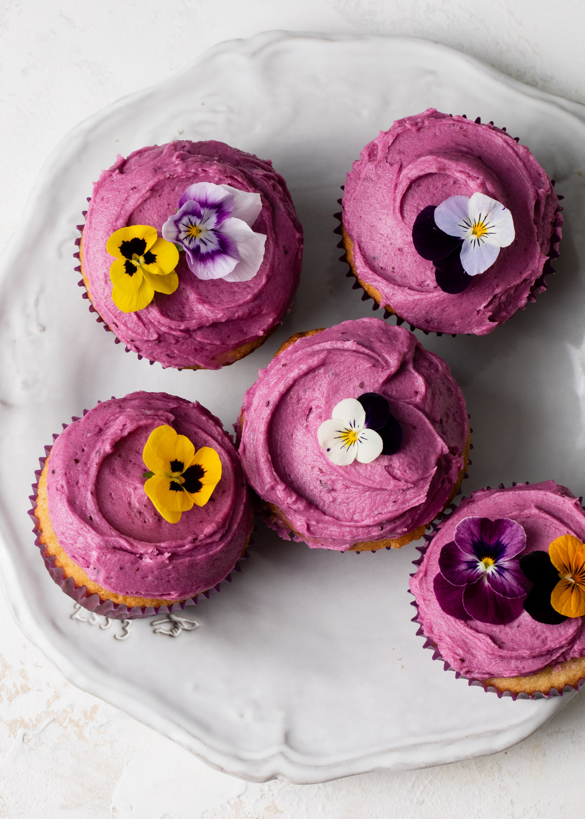 Frosted blueberry cupcakes with purple frosting and edible flowers on top