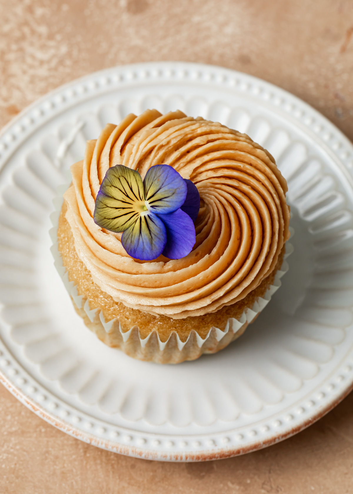 A close up of a swirl of coffee buttercream and edible flower on top