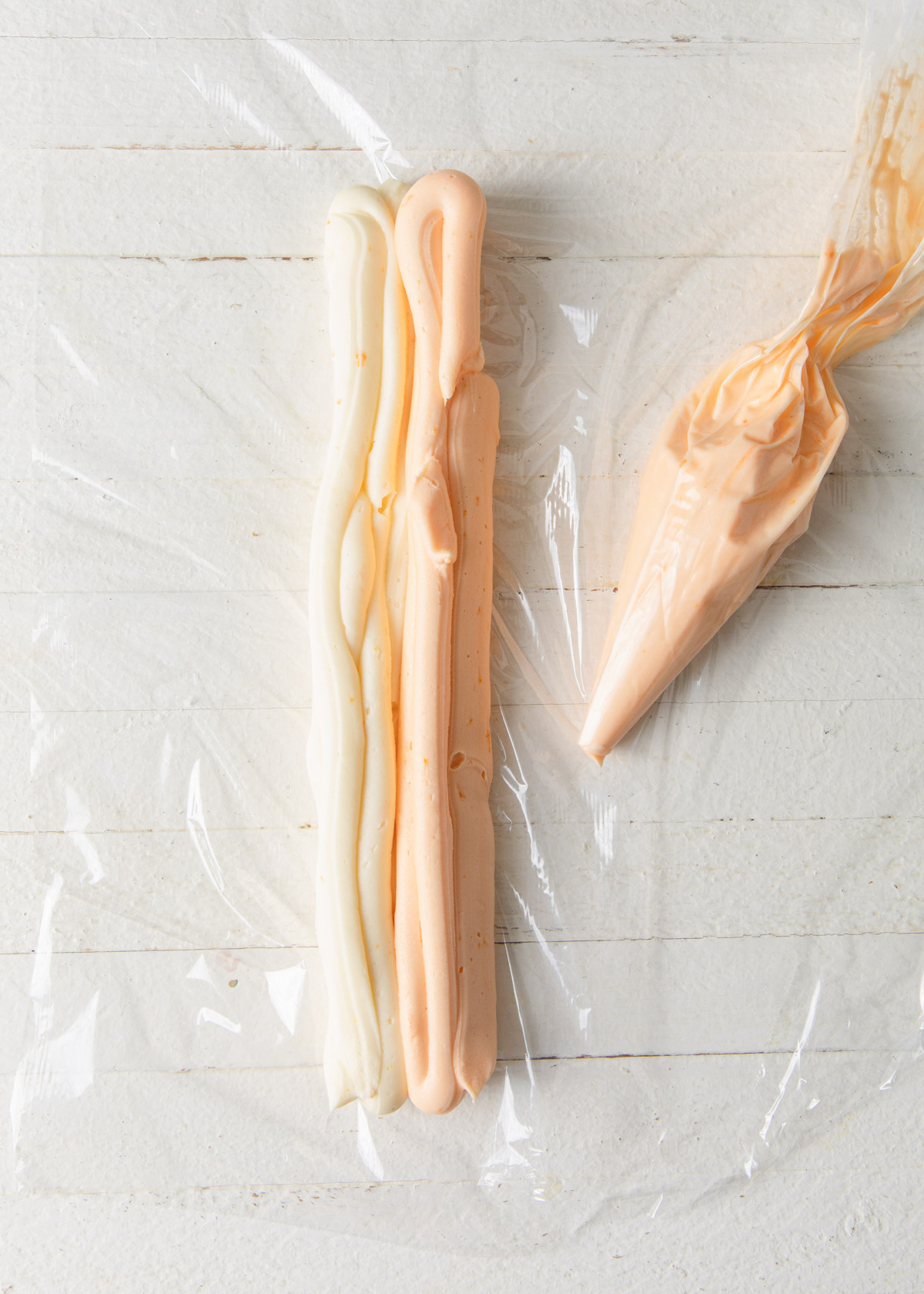 White and orange buttercream in rows on a piece of plastic wrap