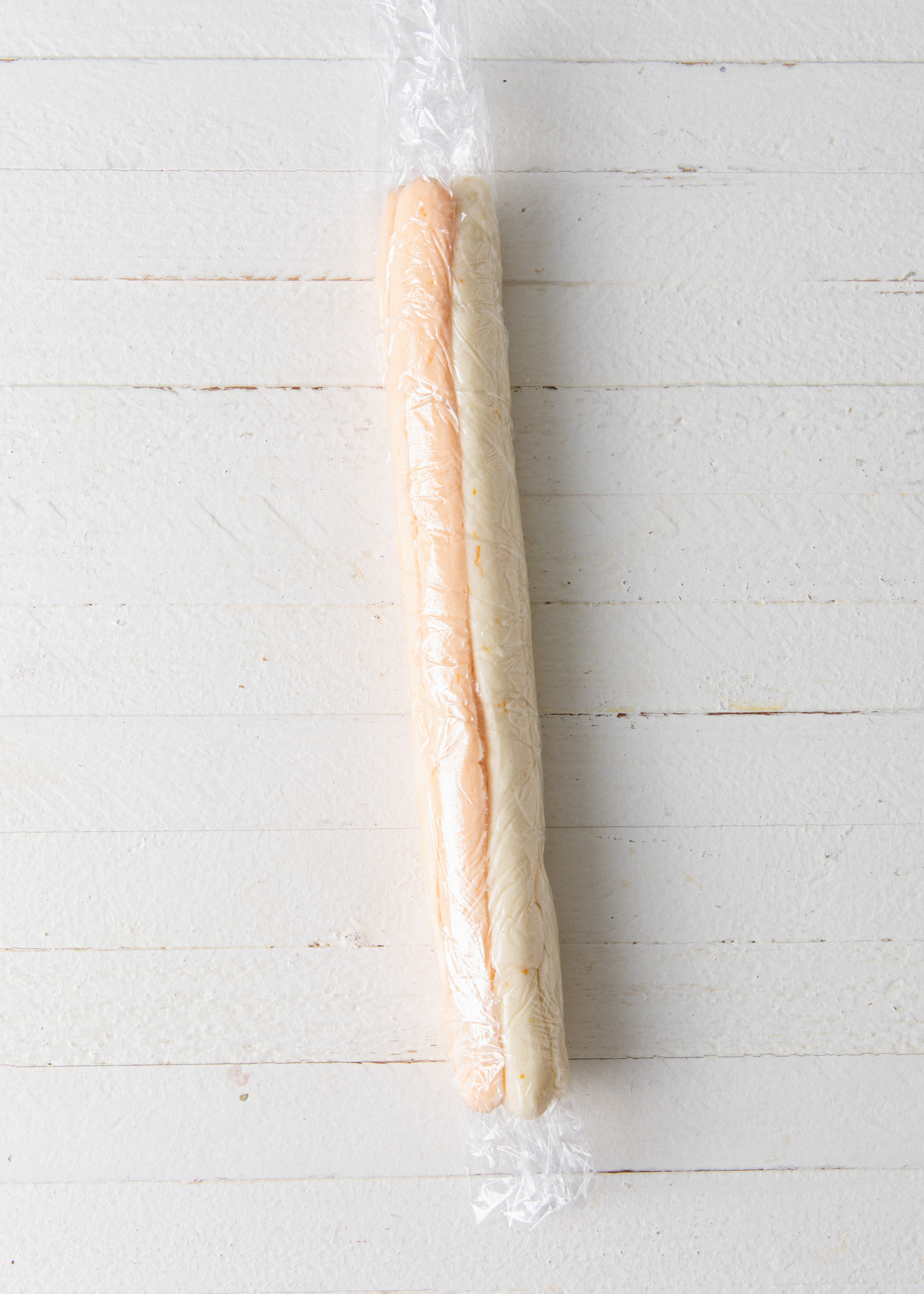 A log of white and orange buttercream wrapped in plastic for a piping bag