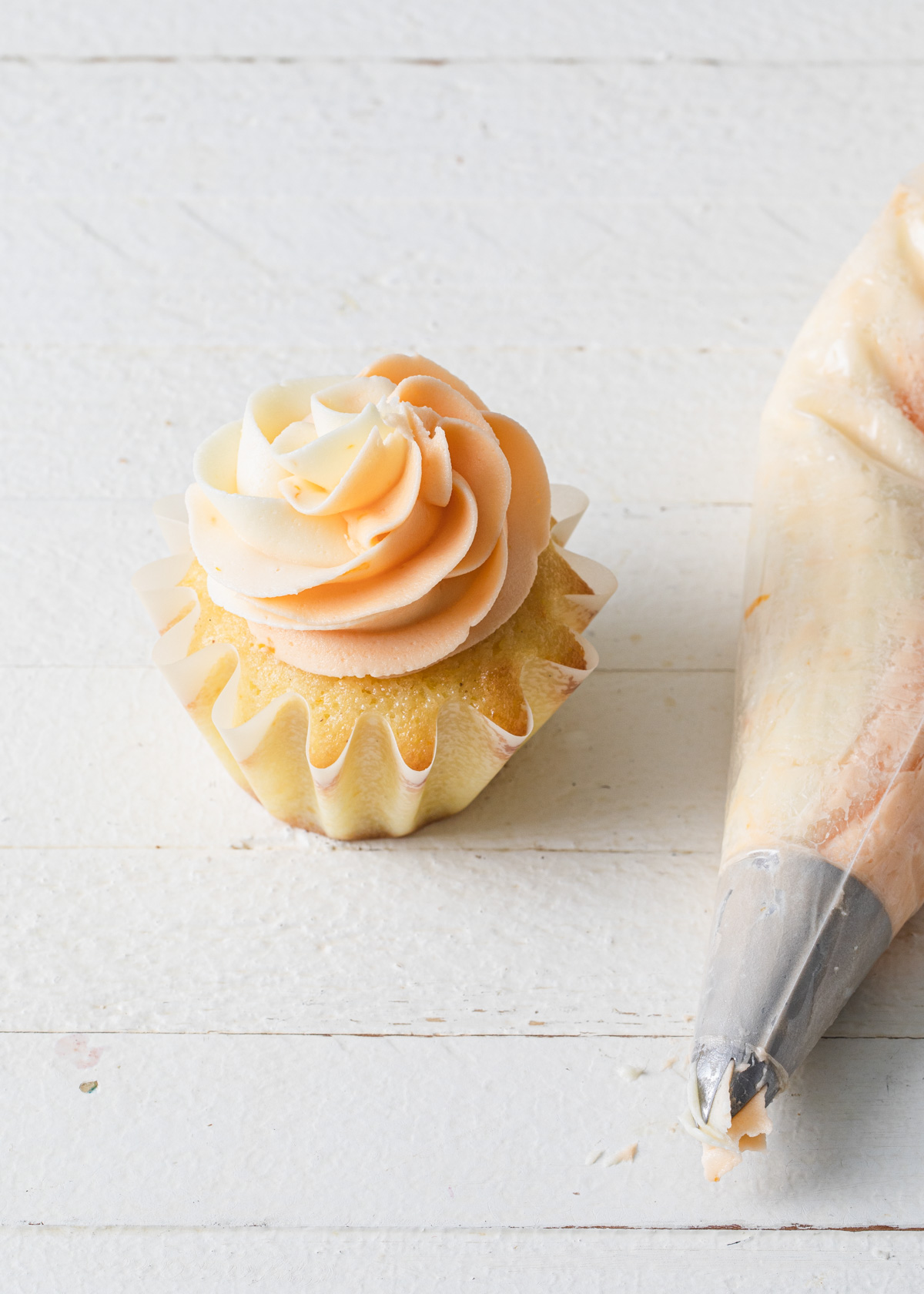 A cupcake with two-tone orange and white buttercream swirled on top