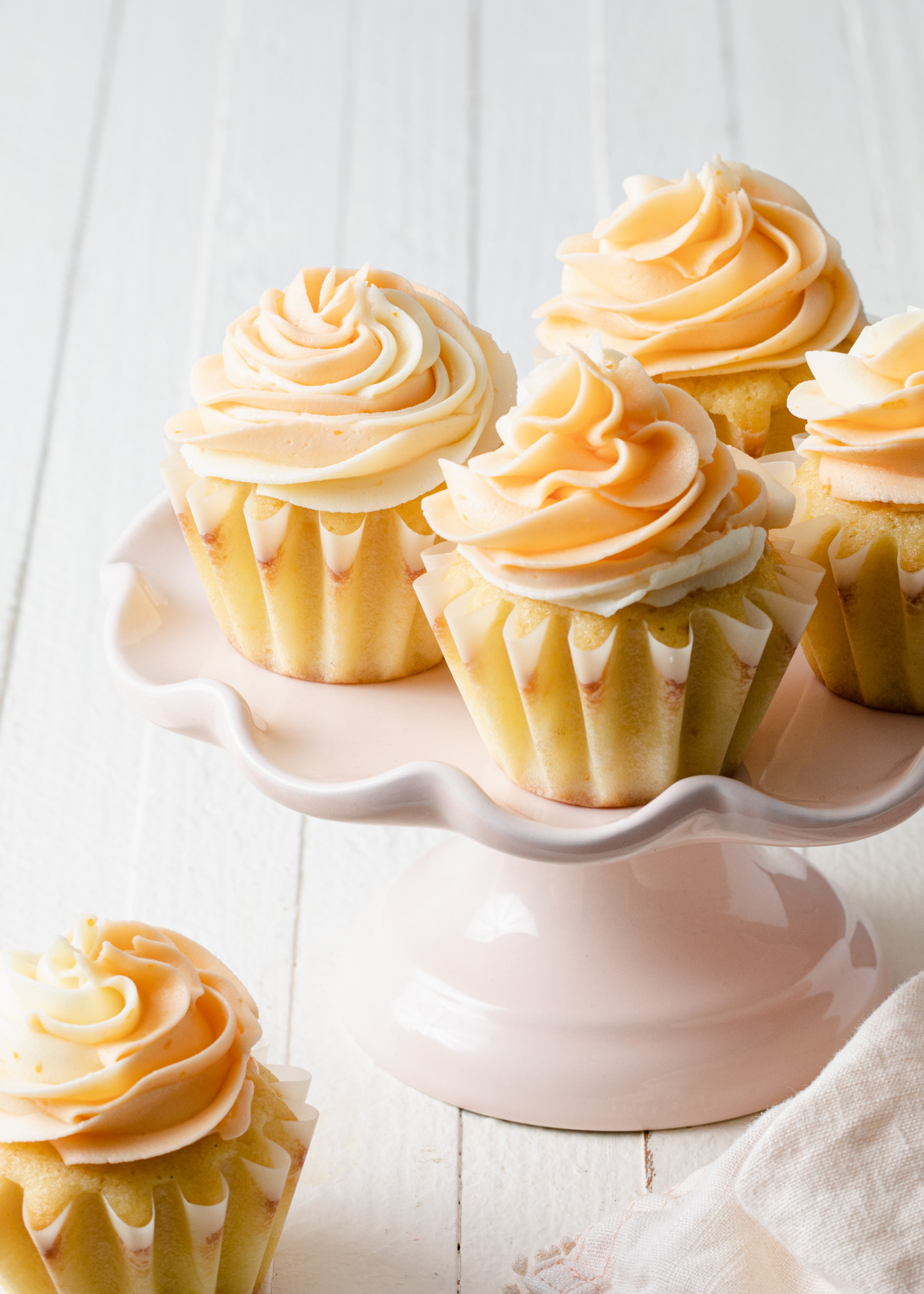 A pink cake stand with orange cupcakes and piped buttercream on top