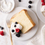 A slice of vanilla chiffon cake with a dollop of whipped cream and fresh berries on top