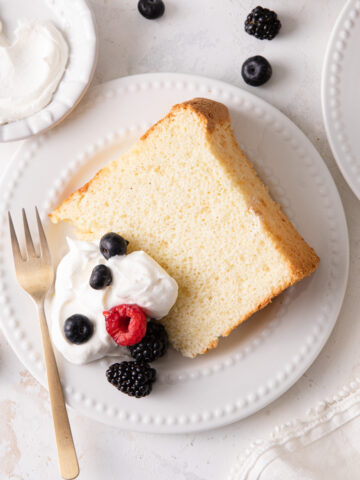 A slice of vanilla chiffon cake with a dollop of whipped cream and fresh berries on top
