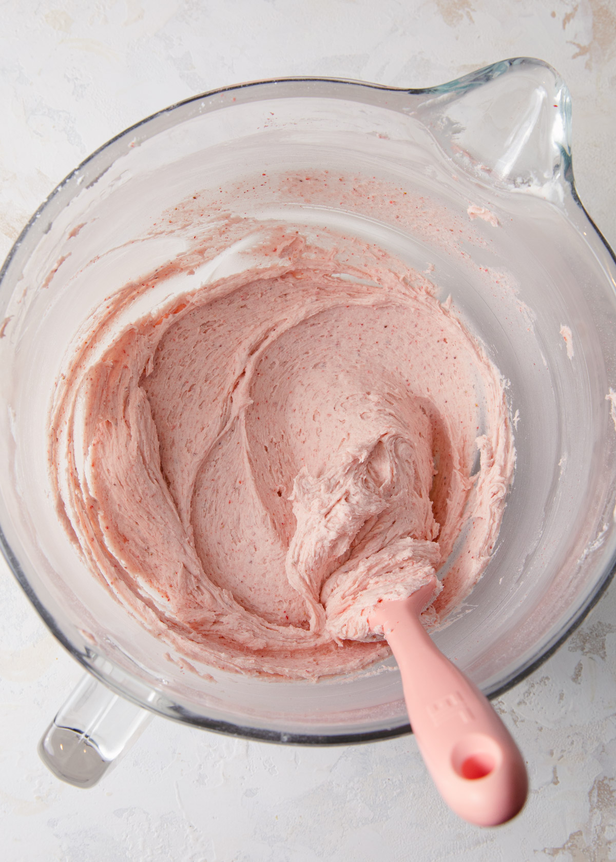 A close-up of strawberry frosting with a pink spatula