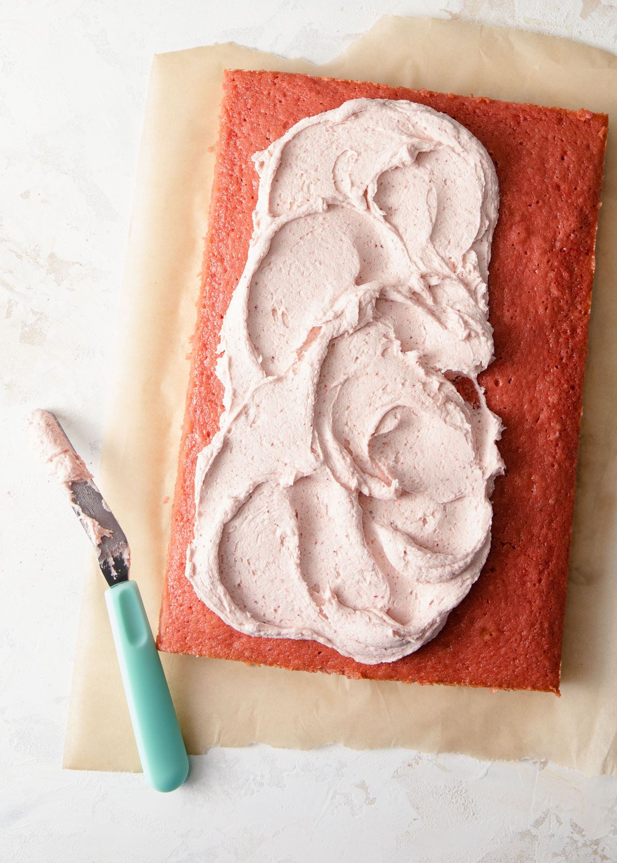 Spread strawberry frosting onto a sheet cake with an offset spatula