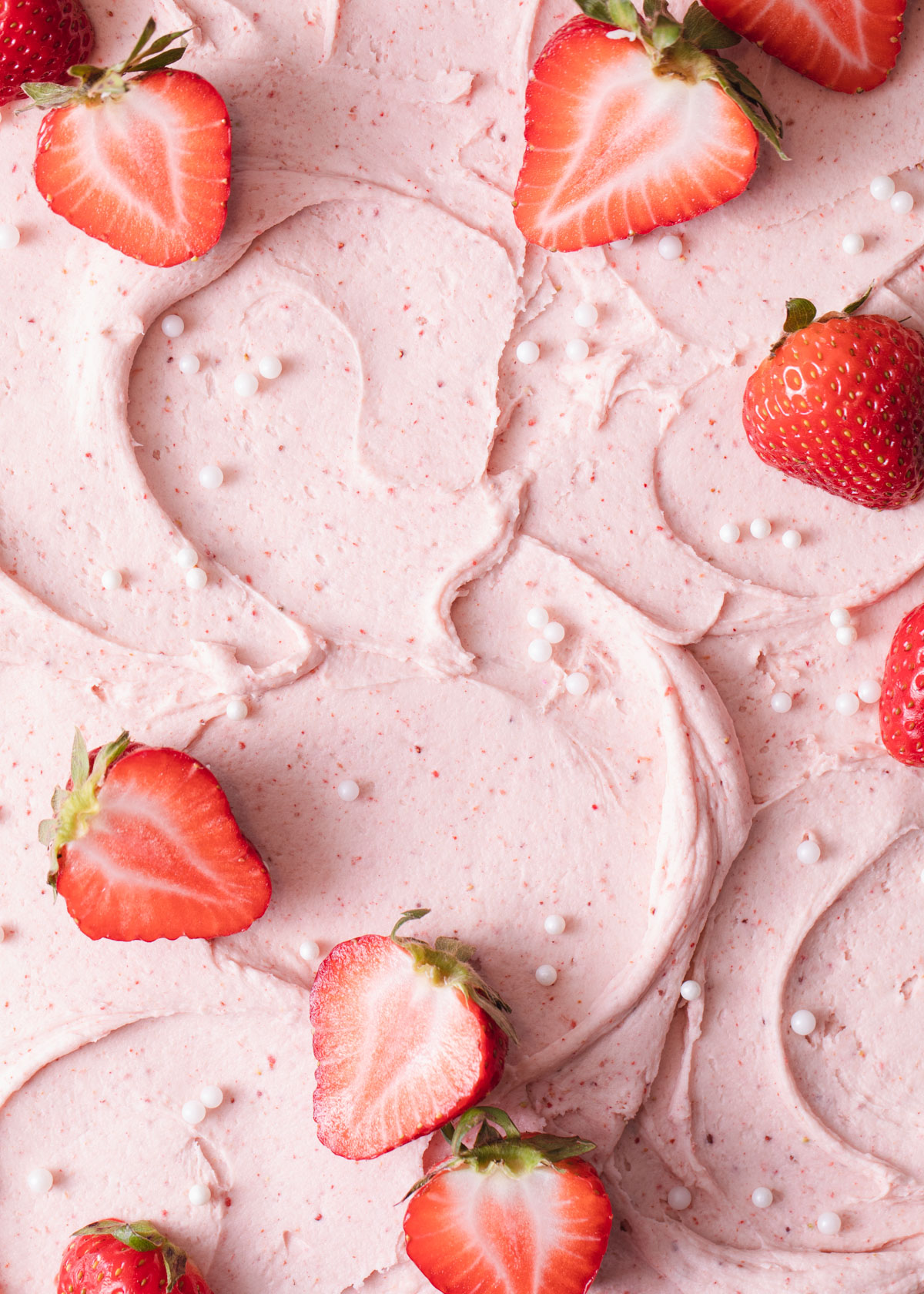 A close-up of strawberry frosting swirled on top of a cake with fresh strawberries on top.