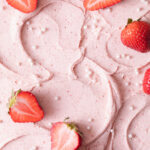 A close-up of strawberry frosting swirled on top of a cake with fresh strawberries