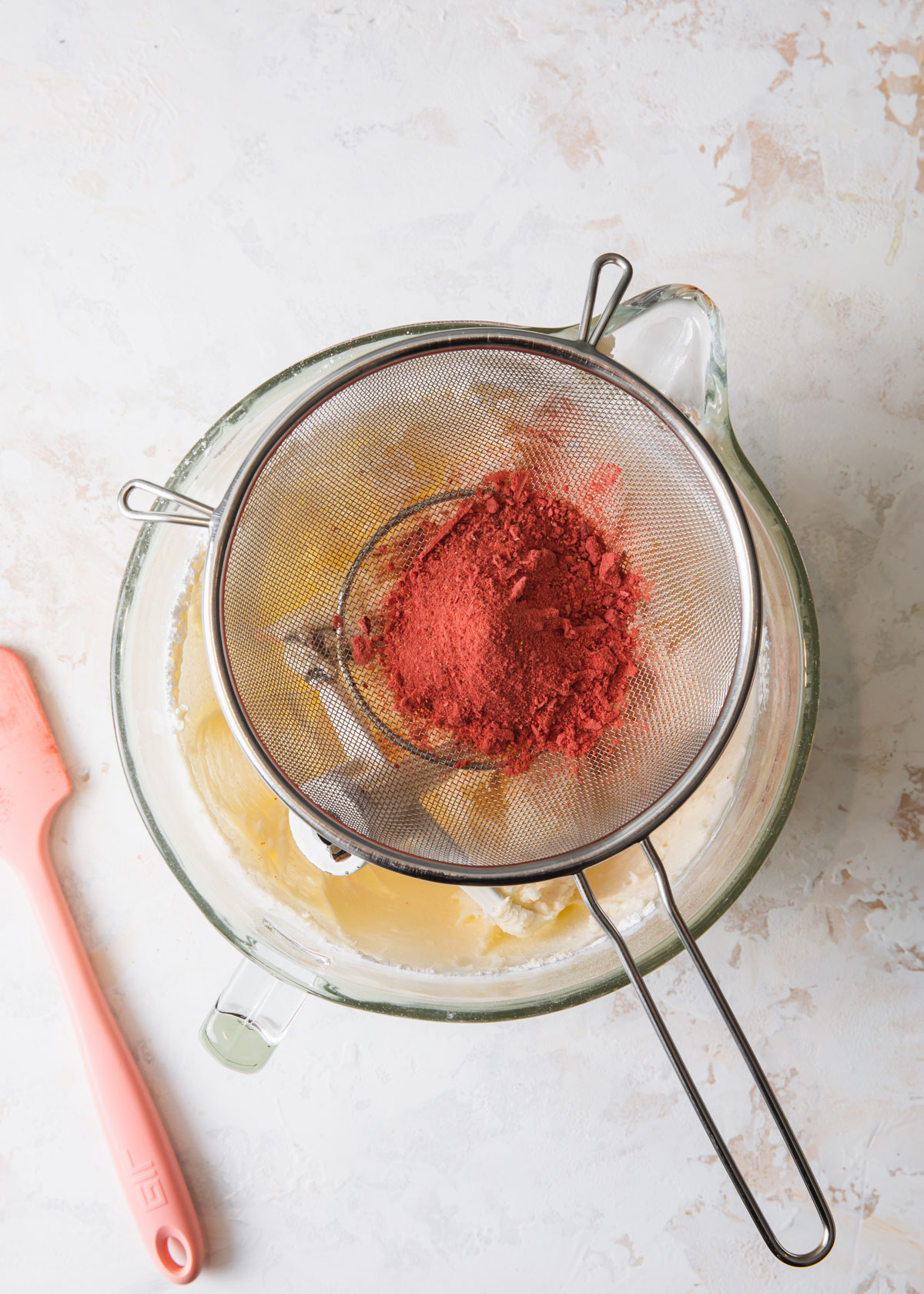 Sifting ground freeze-dried strawberries into a bowl of buttercream