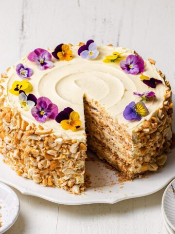 A multi-layered Sans Rival Cake with cashews around the sides and edible flowers on top.