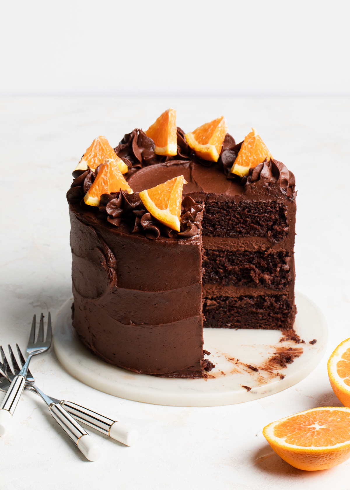 A three-layer chocolate orange cake on a white plate that's been sliced open.