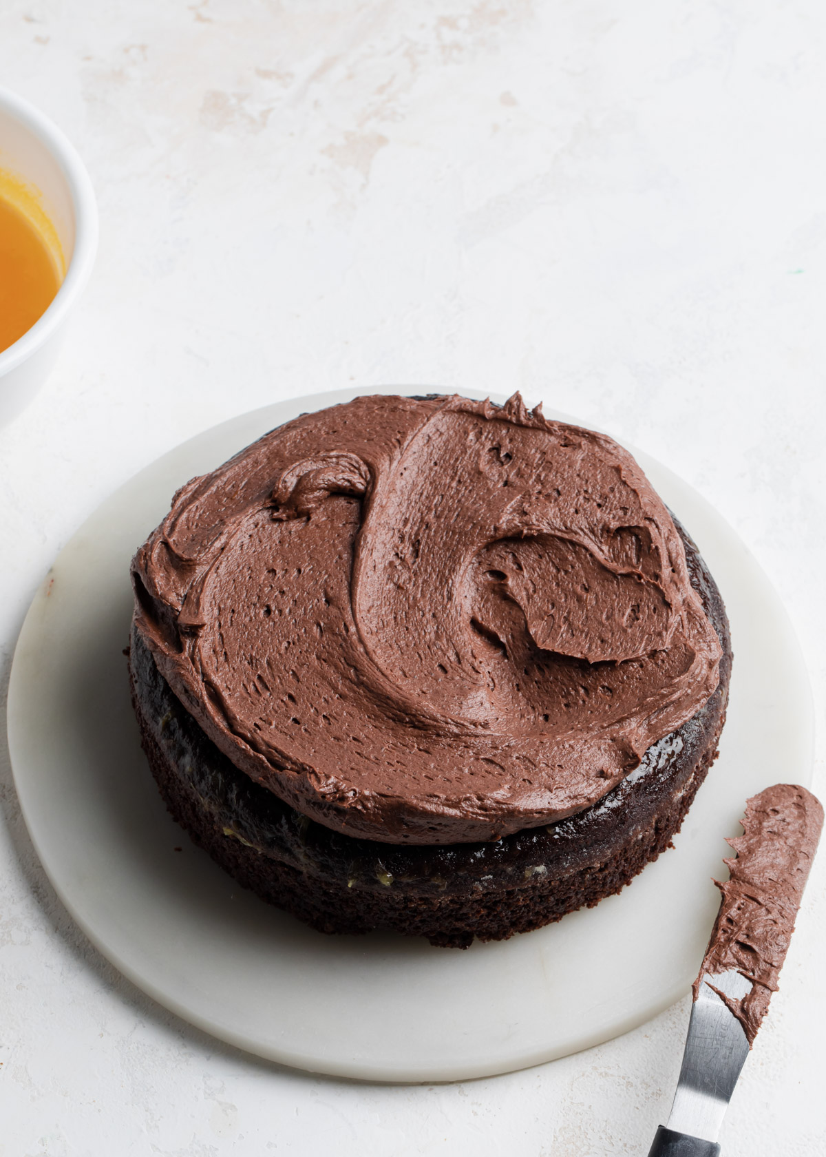 Fudge frosting being spread between layers of chocolate cake