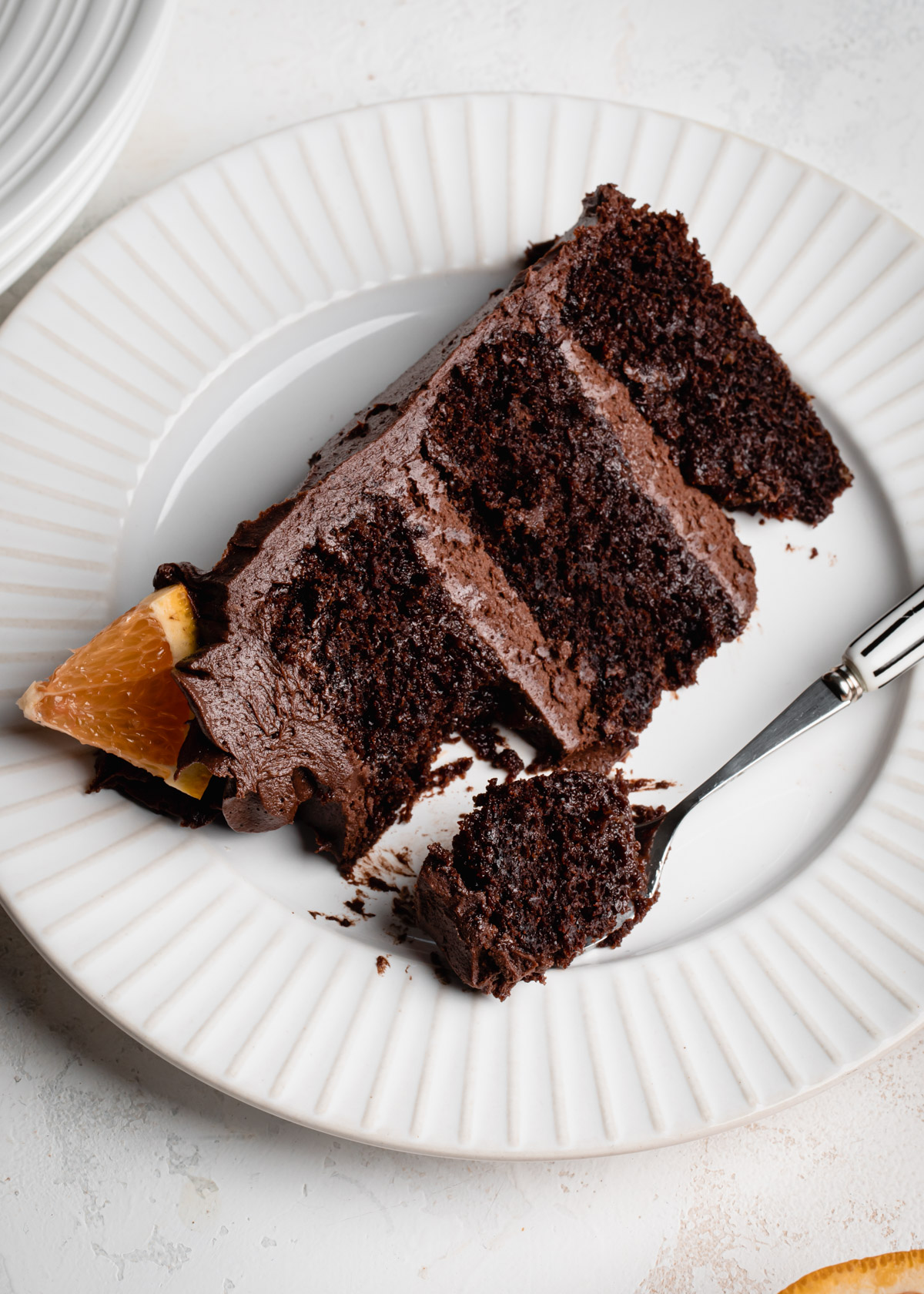 A slice of three layer chocolate orange cake on a white plate with a silver fork