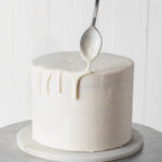Adding white chocolate drip to a cake with a spoon