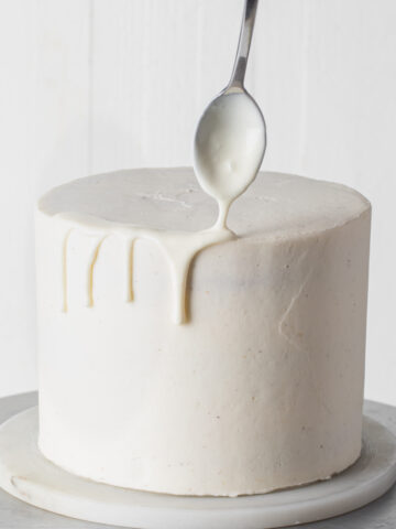 Adding white chocolate drip to a cake with a spoon