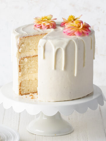 A three layer white velvet cake with vanilla buttercream on a white cake stand that's been sliced into