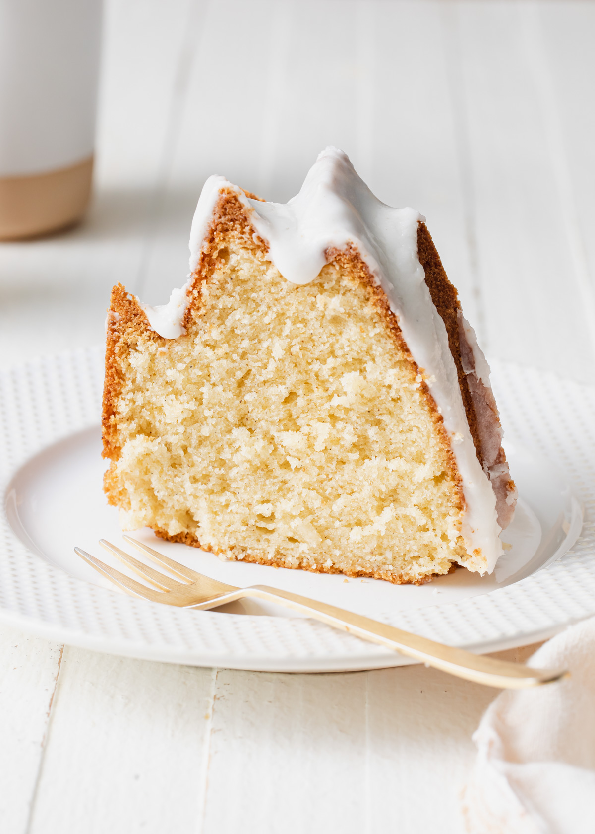 A thick slice of cardamom cake with vanilla glaze on a white plate.