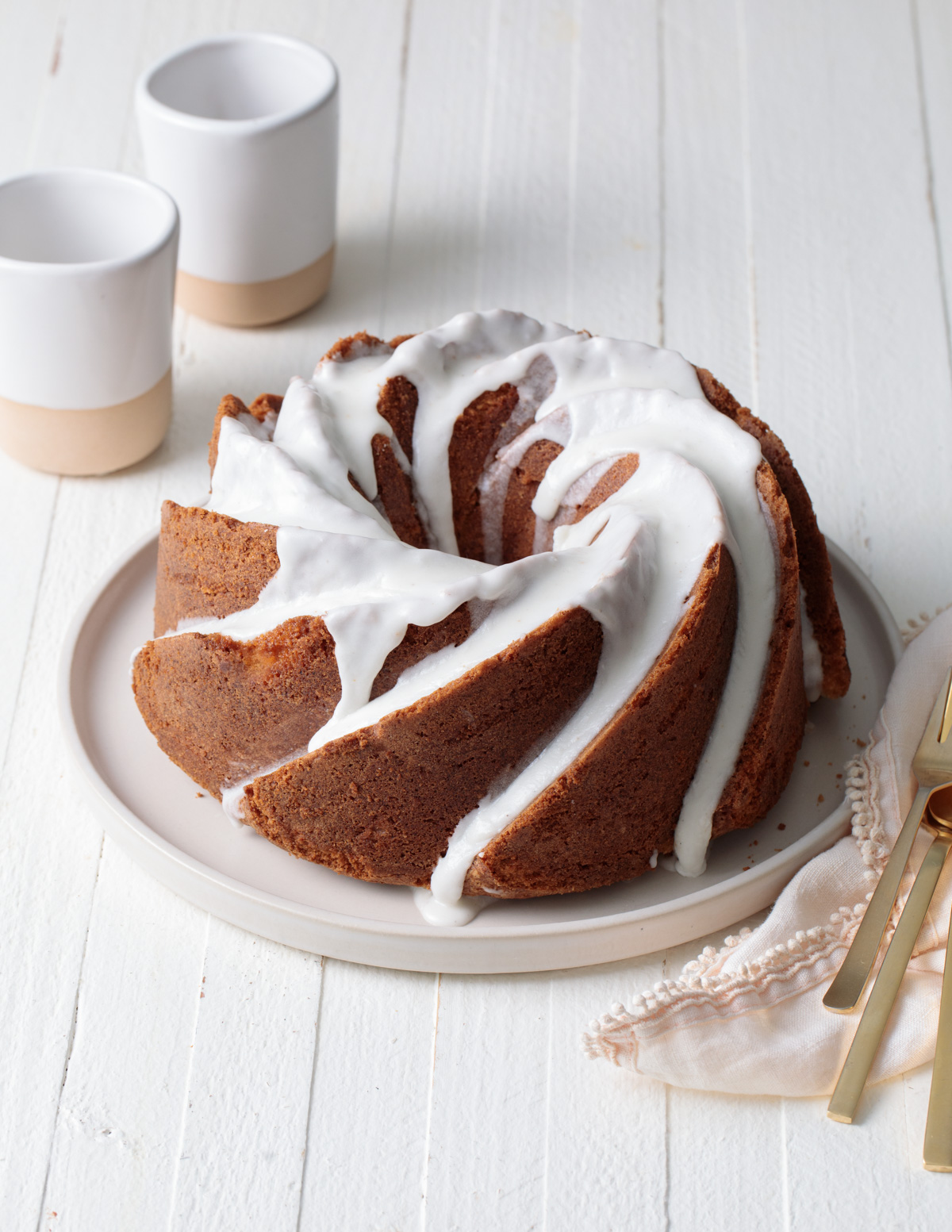 A simple bundt cake with vanilla glaze on top set on a white wood table
