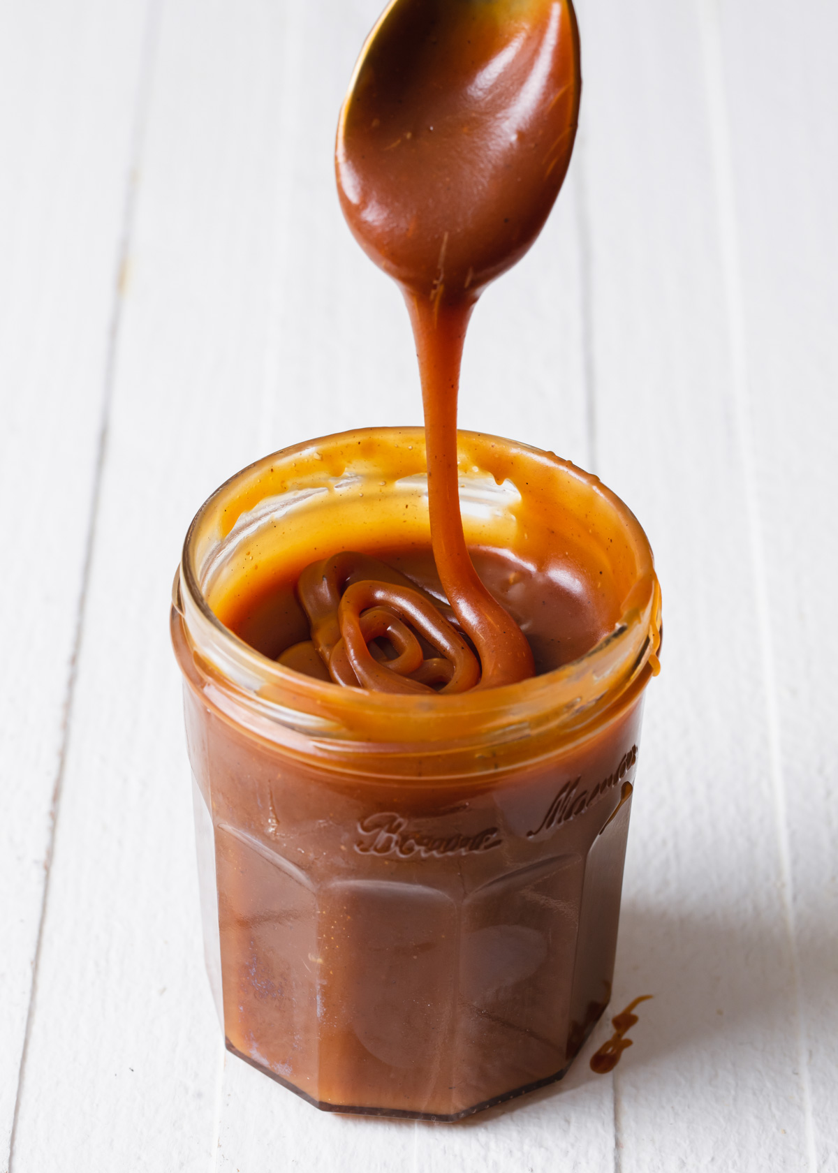 A jar of homemade salted caramel sauce dripping from a spoon