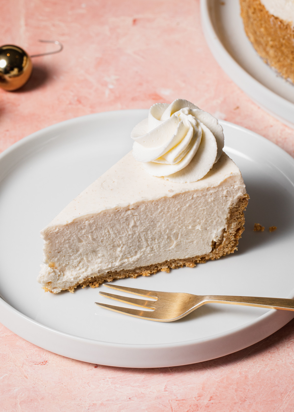 A slice of creamy eggnog cheesecake set on a white plate on a pink tabletop