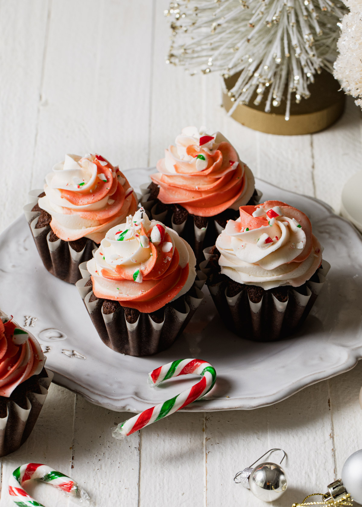 Peppermint buttercream swirled on top of chocolate cupcakes with candy canes and Christmas trees in the background
