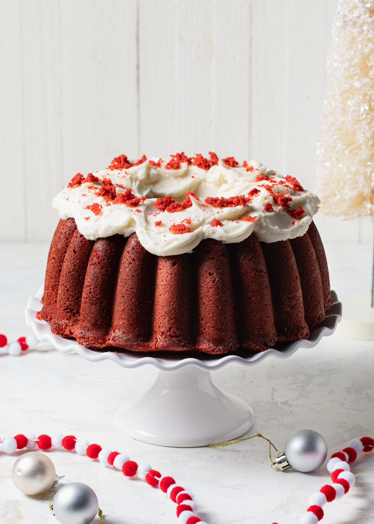 A red velvet Bundt Cake with cream cheese frosting set on a white cake stand