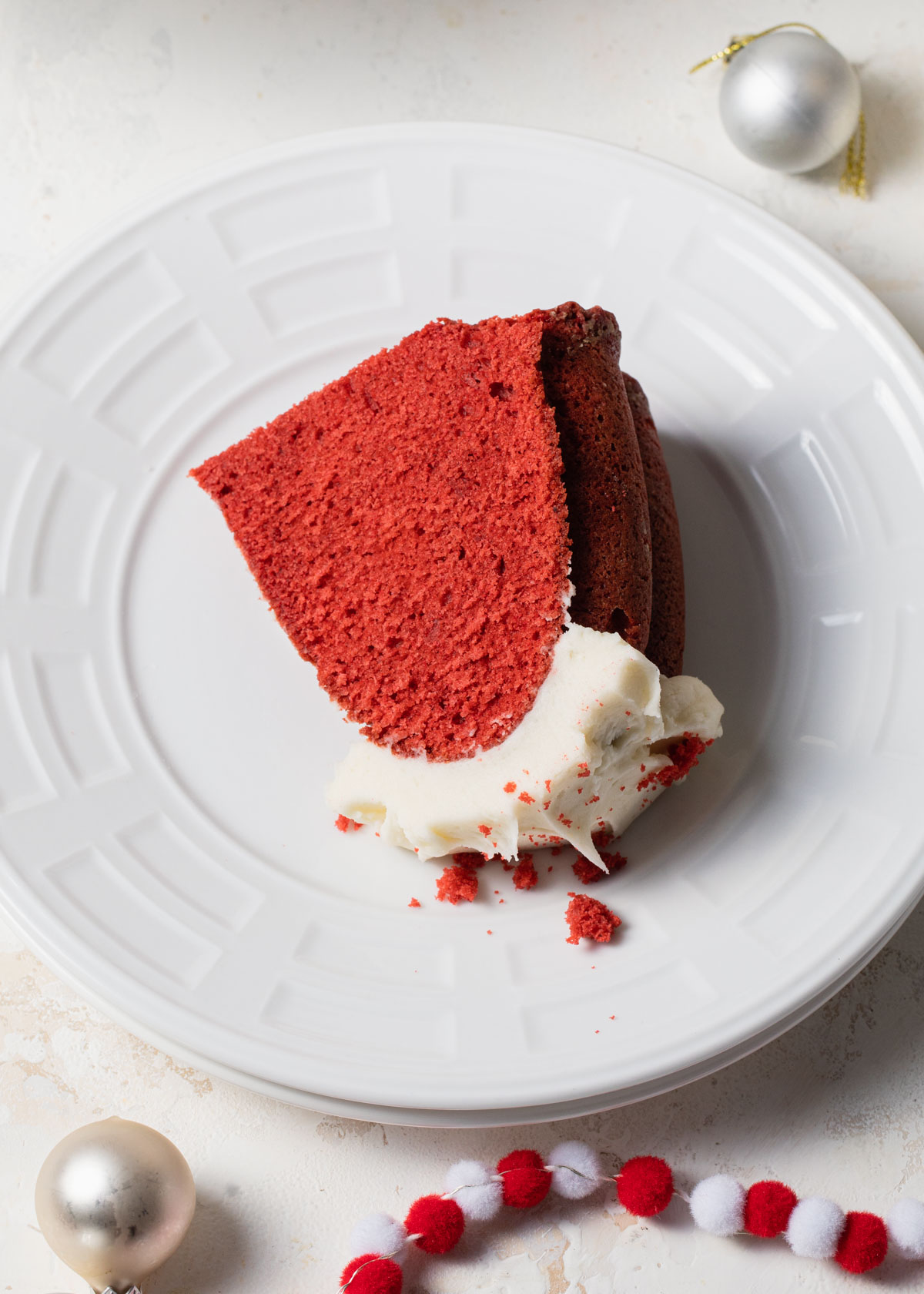 A thick slice of red velvet cake on a white plate with cream cheese frosting