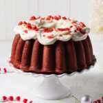 A red velvet Bundt Cake with cream cheese frosting set on a white cake stand
