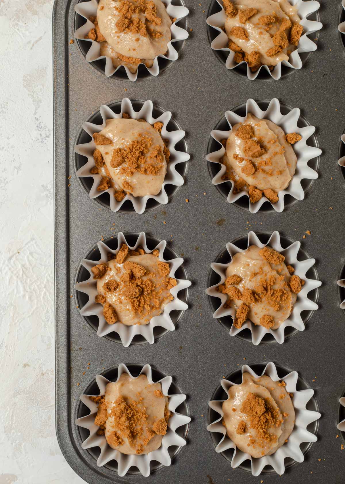 Sprinkles of crushed biscoff cookies on top of cupcakes batter