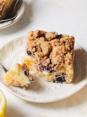 A square of blueberry lemon coffee cake with crumb topping set on a white plate with a fork