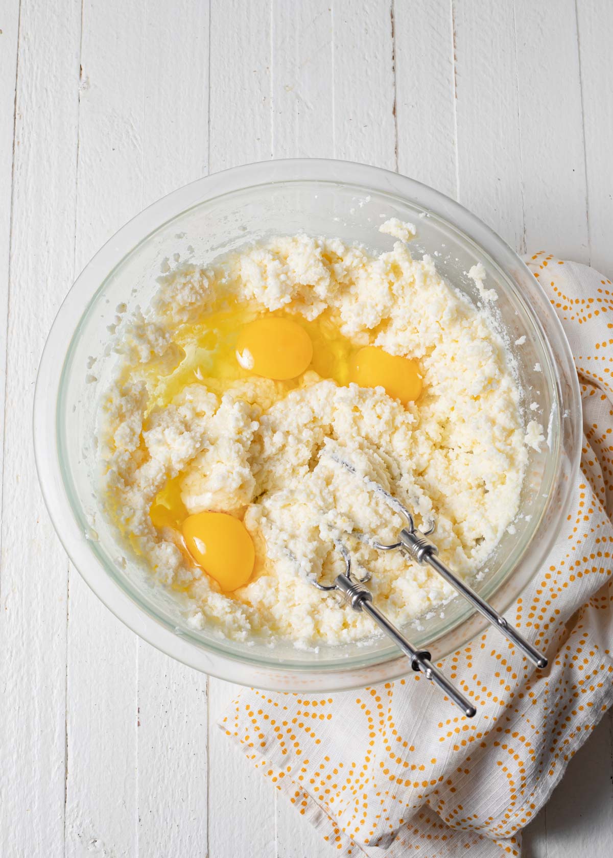 Adding eggs to ricotta cake mixture in a glass bowl