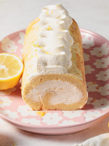 Lemon Swiss Roll cake with piped whipped cream on top set on a pink flower plate.