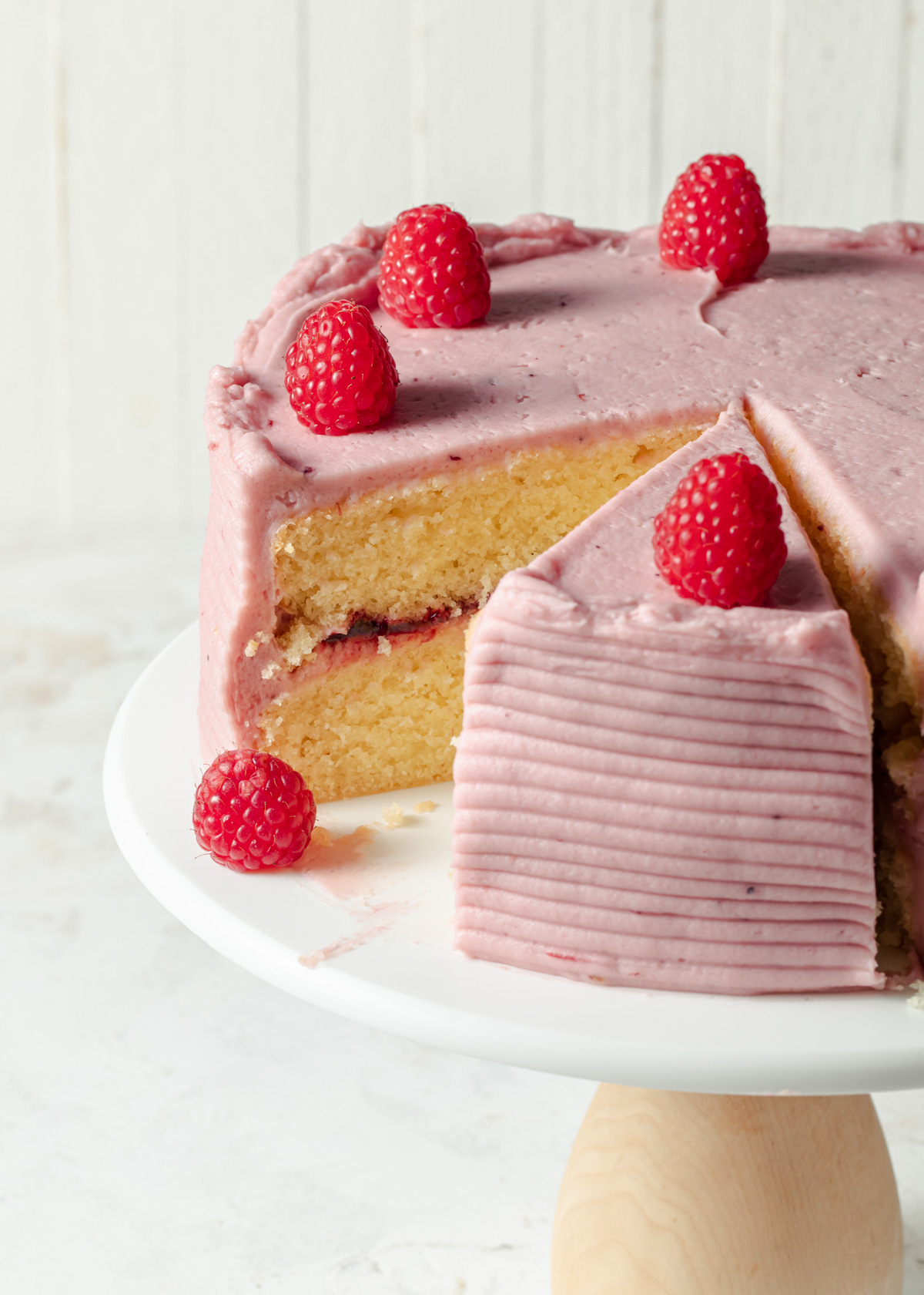 A close-up of a sliced almond layer cake with raspberry frosting and jam filling