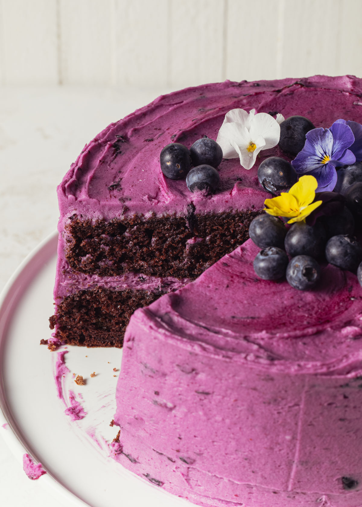 A close-up of a moist chocolate layer cake with blueberry frosting