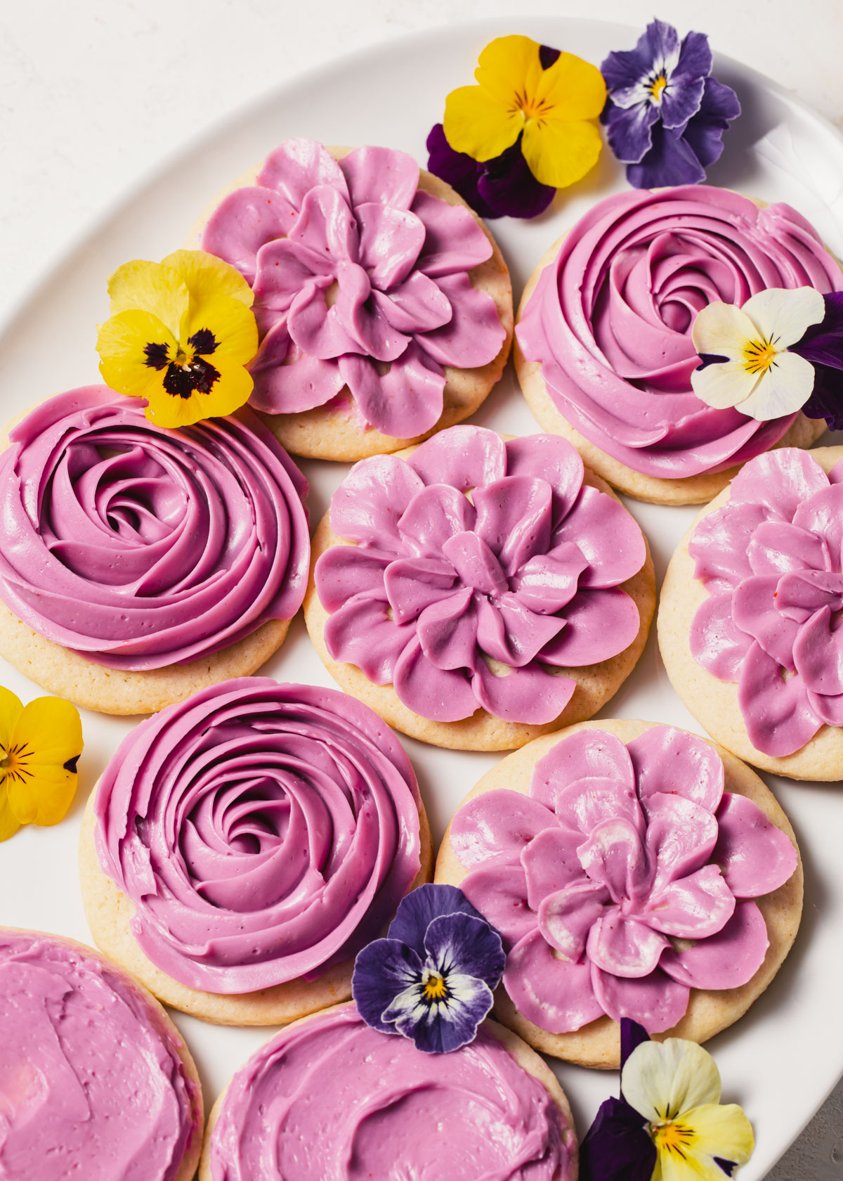 An overhead shot of lemon lavender cookies with lavender buttercream piped on top set on a white plate.