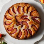 An overhead image of a cake with slices on plum baked in a spiral on top.