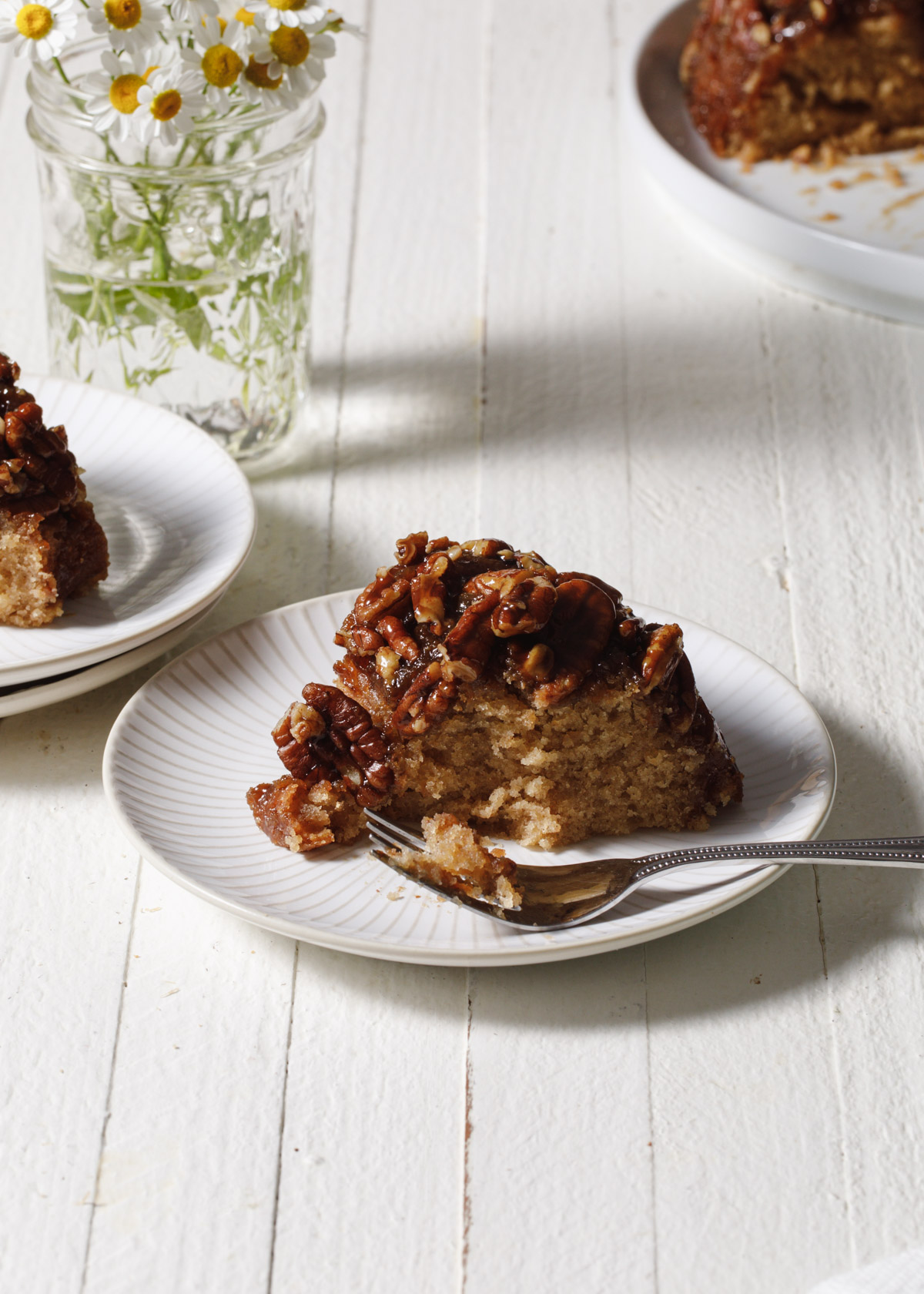 A slice of pecan upside down cake set on a white wooden table with daisies in background