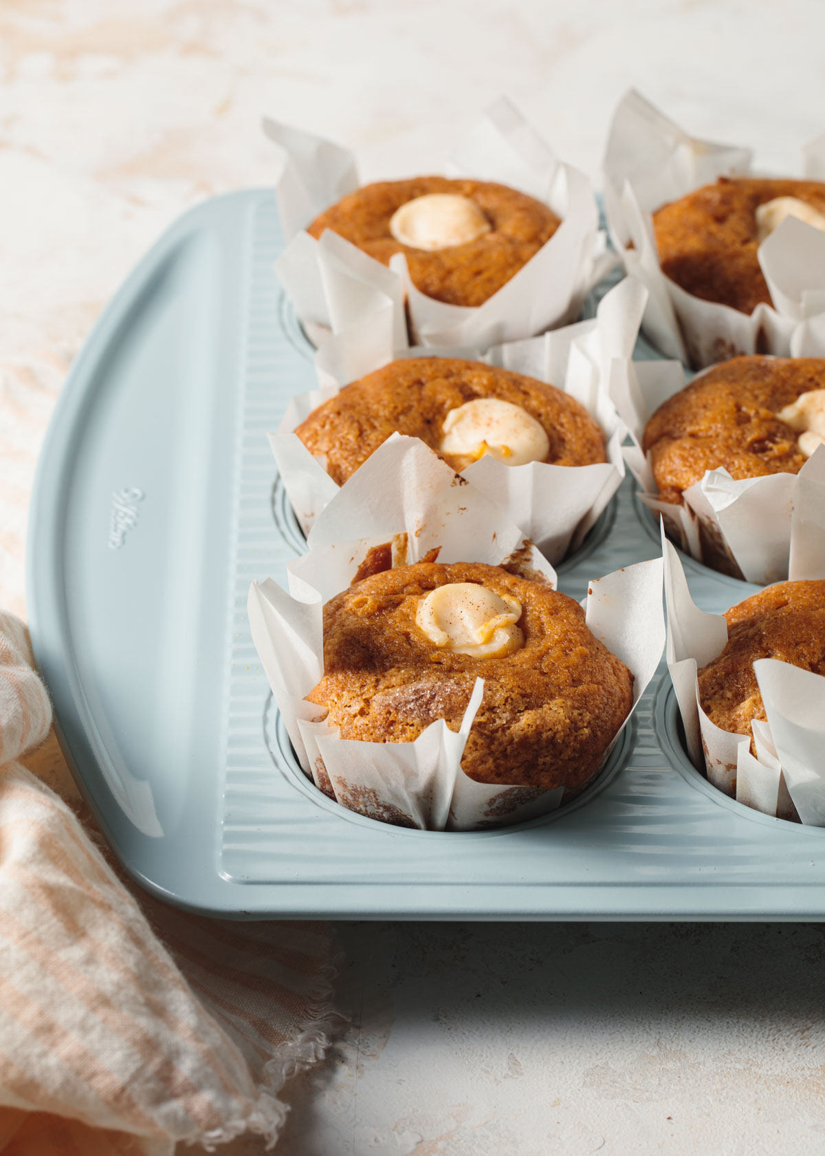 Pumpkin muffins with cream cheese centers baked in a light blue muffin tin