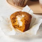 A pumpkin muffin with a bite take out to show cream cheese filling