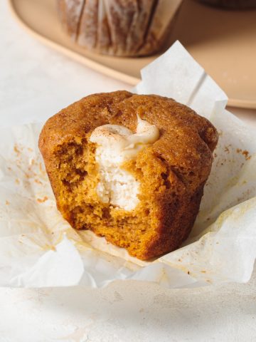 A pumpkin muffin with a bite take out to show cream cheese filling